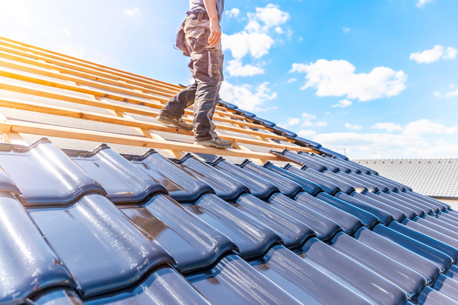 A roofer walking a sun-lit blue tile roof